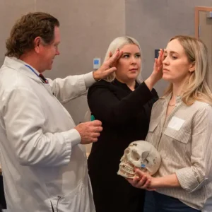 Le Dr Roberts montre à un dentiste comment effectuer la technique de marquage thérapeutique PTIFAT sur une femme qui tient un crâne.